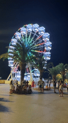 Bar's waterfront night fair: Ferris wheel, market stalls, and street sculptures.