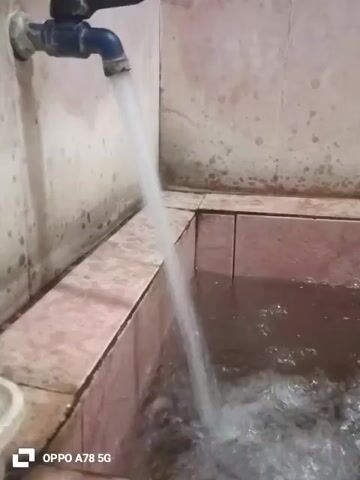 A close-up shot shows a faucet with blue accents running water into a tiled bathtub. The water is a light white color and is splashing as it hits the water already in the tub. The tub is filled with dark brown water. The walls are tiled with light pink tiles. There is visible mildew on the walls above the bathtub. The timestamp appears at the bottom left of the video as "OPPO A78 5G." The video appears to be captured indoors.