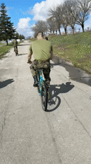 Military personnel cycling on road in uniform