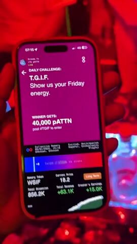 The video appears to be shot in a crowded nightclub. The first shot is close up on a smartphone displaying an app with financial data and a challenge to "show us your Friday energy" for a chance to win tokens. Then the video shows a group of people dancing and standing in a dimly lit nightclub, with colorful stage lights illuminating the scene. A large banner displaying the name of the club is visible in the background. The video captures the vibrant energy and social atmosphere of a nightlife setting.