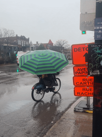 Cyclist uses umbrella while riding through rainy Montreal streets