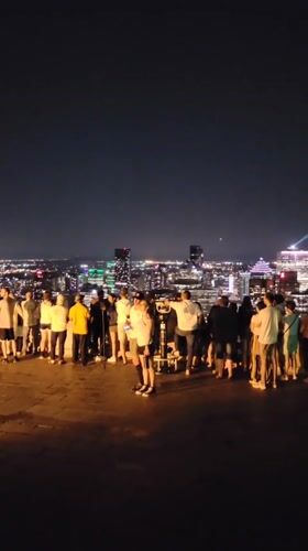 Nighttime crowd takes in the Montreal skyline from an overlook
