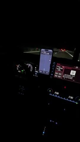 The video shows the interior of a car at night. The driver's side dashboard is visible, with a speedometer reading 133 km/h and a navigation app displayed on a smartphone mounted on the dashboard. The car's infotainment screen is also visible, showing song information. The climate control displays "23.0" for both driver and passenger. The road ahead is visible through the windshield, with other cars and streetlights in the distance. The scene suggests the car is in motion on a highway at night.