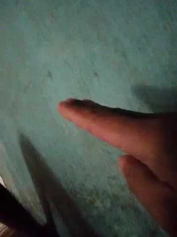 A hand is shown against a blue-green wall. The hand forms different shapes with its fingers: a pointer finger extended, then a thumb and pointer finger extended, then a pointer and middle finger extended in a peace sign, then a pointer finger extended again. The lighting is dim, casting shadows on the wall.