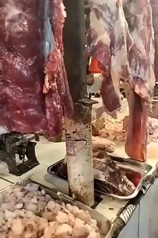 This media file depicts a busy butcher shop or market stall in Bekasi, Indonesia. The scene is filled with raw meat, with large cuts of beef hanging from hooks and smaller portions laid out on counters. Several people are present, including a woman and a child who appear to be customers or interacting with the vendor. The activity suggests a commercial transaction, possibly the purchase of meat.

Notable details include the hanging carcasses of beef, a scale used for weighing produce, and trays filled with chopped meat. The lighting suggests it is daytime, and there are no indications of specific weather conditions. The presence of the scale and the general market atmosphere point to a bustling commercial environment. The interaction between the woman and child suggests a typical shopping experience.

No discernible text is visible in the media file. The overall impression is a vibrant and active market scene focused on the sale of fresh meat.