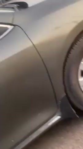 The video starts with a close-up of the front driver's side wheel of a gray sedan. The camera moves up and away to reveal more of the car and then moves onto the street. The view transitions to being filmed from a motorcycle in traffic. A silver hatchback passes by. The viewpoint then shifts to the person riding the motorcycle.