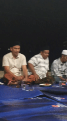 Nighttime communal meal on a blue tarp in Meunasah Bie