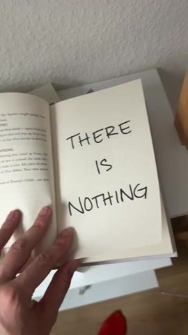 The video shows a person's hands holding open a book. The book's left page contains text in a smaller font. The right page has large, bold, handwritten text that reads "THERE IS NOTHING" on the first page and "WRONG WITH YOU." on the second page. The pages are being flipped from left to right. The book is on a white surface, possibly a shelf, with a wall in the background. The lighting suggests an indoor setting. A person's thumb is visible on the left page, and part of a red shoe is visible at the bottom of the frame.