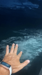 Hand with fitness tracker filmed over foamy ocean water at night
