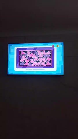 The video displays a television screen with a cartoon program. The first part of the video shows a game where various pink objects are arranged on a grid. The game appears to involve matching or sorting these objects, as they are moved around and rearranged. A green checkmark appears at the end of this segment, indicating success. The second part of the video shows an animation of several red trucks driving on roads that diverge from a central point. This animation is set against a bright blue background with a circular graphic on the left side, which contains some white and orange objects. The overall aesthetic of the program is colorful and child-friendly. The television is mounted on a dark wall, suggesting an indoor setting. There is no information about the time of day, weather, or specific emotions being conveyed. The only visible text is a logo in the upper right corner of the screen, which appears to be a stylized "3" within a circle, possibly indicating a channel or program number. The context provided indicates the location is Melitopol, Ukraine.