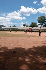 Young people play volleyball on dirt court in Kenya