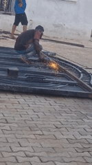 Man grinds metal gate outside building, sparks fly