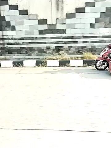 The video shows a street scene. First, a blue motorcycle speeds along the street. Then, a red motorcycle with a sidecar travels past. Finally, the video shows people standing near motorcycles under a bridge.