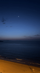 Crescent moon over calm Calp coastline at dawn