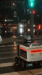 Delivery robot waits at Moscow crosswalk during evening rain