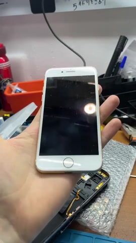 The video shows a person's hand holding a gold iPhone. The phone is partially disassembled, with the front panel removed. The person rotates the phone to show different angles. The background appears to be a workbench with various tools and electronic components.