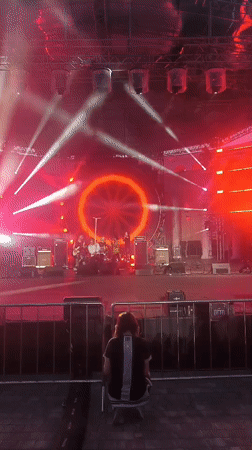 Outdoor concert at dusk, red-lit stage with circular backdrop