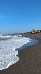 Beachgoer enjoys waves at Indonesian black sand shore