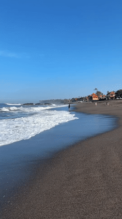 Beachgoer enjoys waves at Indonesian black sand shore