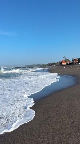 Beachgoer enjoys waves at Indonesian black sand shore