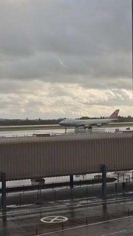 The video shows a China Airlines Cargo plane, likely a Boeing 747, moving on a wet runway at an airport. The plane's full markings are visible, and it's seen from a slightly elevated position, possibly a terminal or another airport building. A covered walkway or bridge is visible in the foreground, partially obstructing the view of the runway. The weather appears overcast, with a cloudy sky. The surface near the camera is wet, suggesting recent rain. There are few other details visible beyond the plane and immediate airport surroundings.