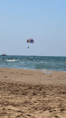 Parasailing, strolling, and boats on a calm beach day