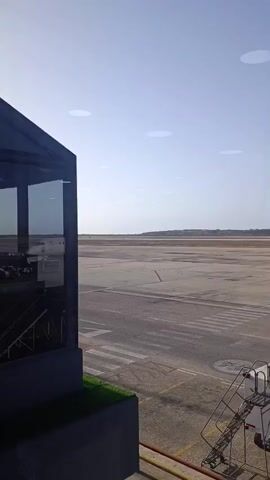 The video shows a plane, labeled "Conviasa," parked on a tarmac at an airport on a sunny day. The camera pans from an unobstructed view of the airport runway to focus on the plane as it sits stationary near a staircase and luggage cart. The camera appears to be inside the airport.