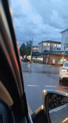Driving through rain at dusk, city streets slick and lit