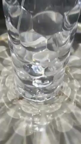 The video shows a clear glass vase sitting on a surface. The vase has a textured, almost honeycomb-like pattern on its exterior. Light shines through the vase, casting a pattern of concentric circles on the surface beneath it. The surface appears to be made of marble or a similar material. The top of the vase is open and dark inside. The camera moves slightly, changing the angle of the shot.