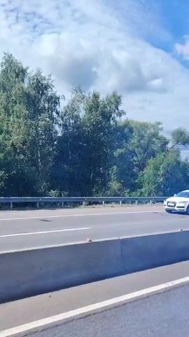 A car drives past trees and buildings next to a highway.