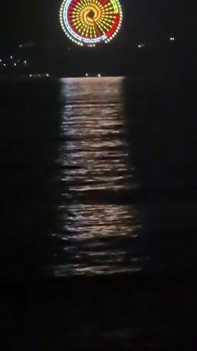 Lit Ferris wheel reflects across water in Nha Trang