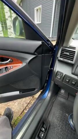The video shows the interior of a car, specifically the driver's seat of a Toyota Camry. The driver opens the car door and enters the car. The camera focuses on the steering wheel and the dashboard. The driver inserts the key into the ignition and starts the car. The dashboard lights illuminate. The video shows a suburban environment with a house and trees visible through the windshield.