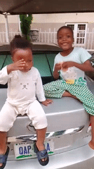 Two children play around silver car in residential courtyard