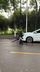Person with leaf blower walks wet street in Jiangjin