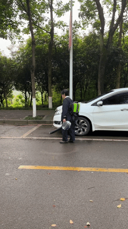 Person with leaf blower walks wet street in Jiangjin