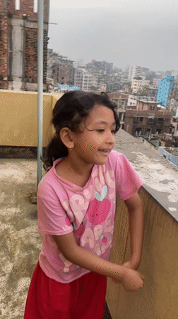 Rooftop afternoon in Dhaka, plants, dancing, flooded streets below