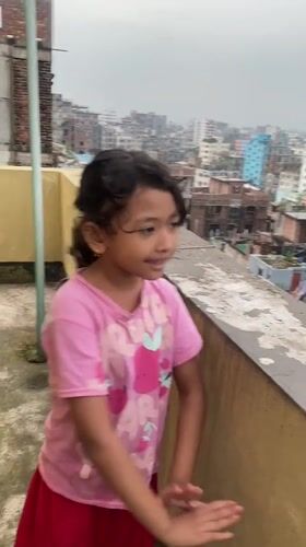 Rooftop afternoon in Dhaka, plants, dancing, flooded streets below