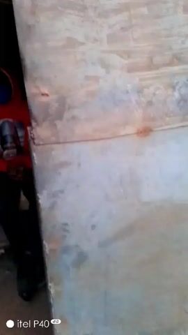 The video shows someone walking through a small, dark space with wooden walls and shelves, then exiting into an outdoor area with a dirt ground and a fence. A person in a red shirt is visible inside the dark space. The camera movement is shaky, and the video is brief. The outdoor area has a walled enclosure and a gray metal fence.