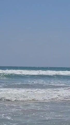 The video shows a clear blue sky meeting a calm ocean with gentle waves lapping at the shore. The water is a translucent blue-green, and the waves are small and foamy. The scene is tranquil and serene, conveying a sense of peace and relaxation. The sun appears to be shining brightly, reflecting off the water's surface. No people or objects are visible in the video, only the natural beauty of the ocean and the sky.