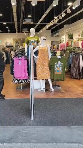 The video shows the entrance to a clothing store. A woman is standing in the doorway, facing the camera. She is wearing a black t-shirt and black and white striped pants. She is smiling and waving. The store is well-lit and stocked with clothing. The store's name, "Yours," is visible above the entrance.