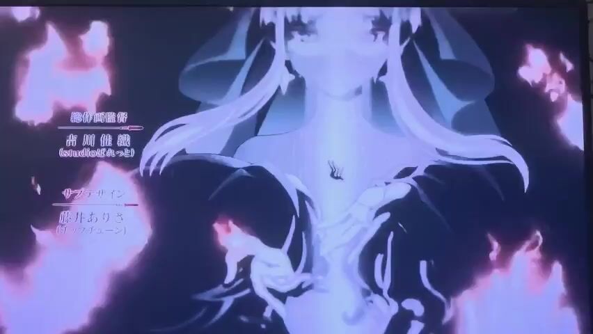 The video displays a scene from an anime. In the foreground, two silhouetted figures, one appearing female with long flowing hair and the other with short hair, are facing each other. They are bathed in a purple and pink ethereal glow, with abstract flame-like patterns emanating from behind them. Text is visible on the left side of the screen, indicating credits in Japanese. The scene appears to be a title card or end credit sequence.