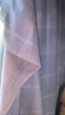 The video shows a close-up of a navy blue curtain with a subtle plaid pattern. The curtain is partially drawn, revealing a blurred view of trees and greenery outside, suggesting it is daylight. The outside scene is out of focus and appears to be moving, indicating the viewer is likely inside a vehicle. The lighting is natural and diffused. There are no people or clear objects visible in the scene.