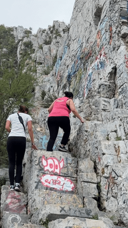 Two women climb graffitied rocky slope in Santa Catarina