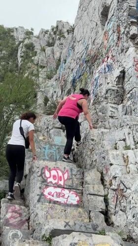 Two women climb graffitied rocky slope in Santa Catarina