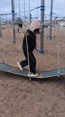 Girl crosses suspended playground walkway using rope handholds for balance
