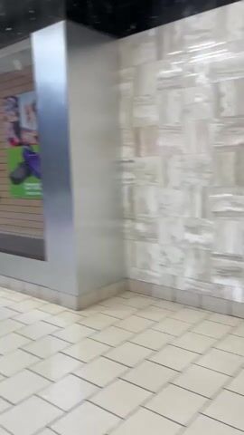 The video pans across the interior of an empty retail space. The floor is tiled with a repeating pattern of light-colored squares. The walls are decorated with various materials, including what appears to be wood paneling, stone, and a large poster advertising Crocs footwear. There are shelves and display cases visible, but they are empty. The overall impression is that of a vacant storefront.