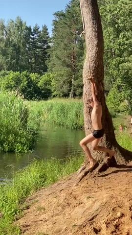 A boy swings from a rope attached to a tree over a body of water. He lets go of the rope and jumps into the water, creating a splash. He then swims in the water. The background consists of trees and tall grass.