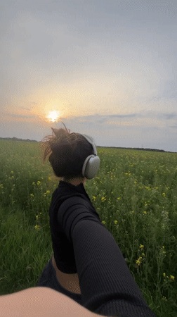 Woman records selfie walk through flowering fields at sunset