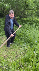 Man cuts grass with scythe in rural Russian village