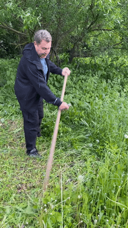 Man cuts grass with scythe in rural Russian village